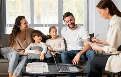 A family of four sits on a sofa, discussing debt consolidation with a bankruptcy attorney in Sulphur Springs; a laptop and documents are on the table in front of them.