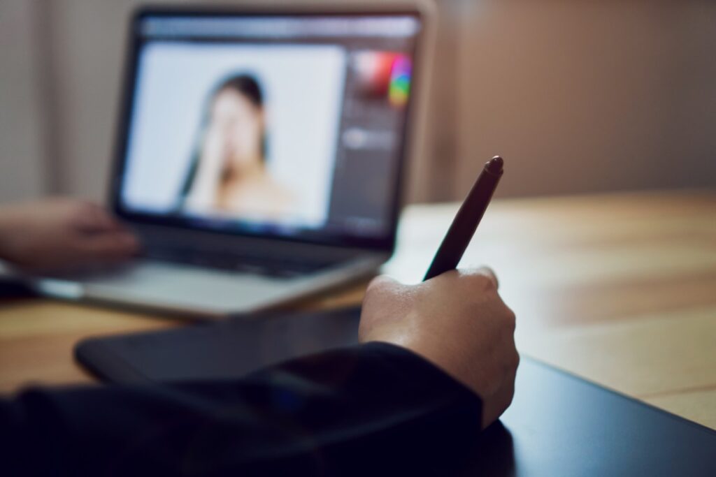 A person using a digital pen and tablet edits a photo of a woman on a laptop, with their blurred hand and workspace in the background—much like how a bankruptcy attorney in Sulphur Springs helps clients edit their financial picture.